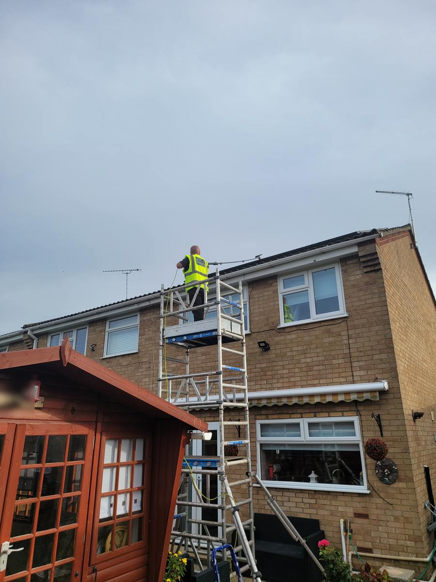 Operative on an access tower cleaning the gutter and fascia at the rear of a two-storey brick house