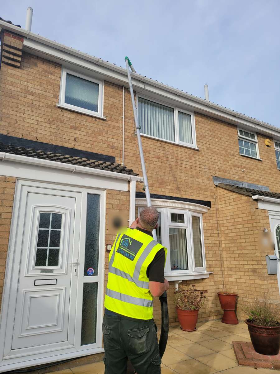 Operative in a DB hi-vis vest using a tall gutter vacuum pole on a two-storey brick house